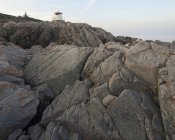 Rochas costeiras rachadas com pequeno farol no topo — Fotografia de Stock