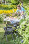 Женщина накрывает стол в саду, освещенном солнцем — стоковое фото