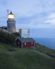 Illuminated lighthouse on green hill at dusk — Stock Photo