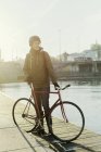 Homme adulte moyen debout avec vélo à engrenages fixes sur jetée — Photo de stock