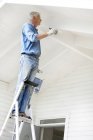 Senior man standing on ladder and painting wall — Stock Photo