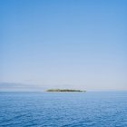 Далекий вид на зеленый остров в море под голубым небом — стоковое фото