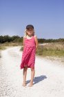 Девушка в розовом платье стоит на грунтовой дороге — стоковое фото