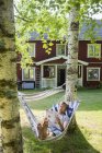 Mann liest in Hängematte gegen Ferienhaus — Stockfoto