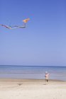 Хлопчик літає повітряним змієм на пляжі, вид ззаду — стокове фото