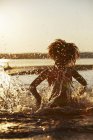 Вид спереду дівчина бризкає в озері на заході сонця — стокове фото