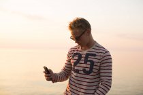 Человек в очках с помощью смартфона у озера, сосредоточиться на переднем плане — стоковое фото