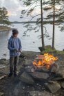 Menino fazendo fogueira pelo lago Harsjon ao pôr do sol — Fotografia de Stock