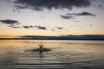 Silueta de hombre con los brazos levantados nadando en el mar - foto de stock