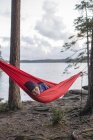 Boy lying in hammock by lake at sunset — Stock Photo