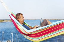 Man lying in hammock and using laptop, focus on foreground — Stock Photo