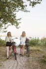 Visão traseira de duas meninas adolescentes andando com bicicletas — Fotografia de Stock