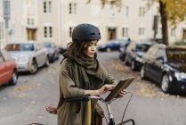 Молода жінка використовує цифровий планшет, стоячи на велосипеді — стокове фото