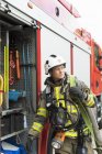 Feuerwehrfrau mit Ausrüstung steht neben Feuerwehrauto — Stockfoto