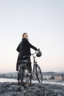 Young woman standing by bicycle on rock, focus on foreground — Stock Photo