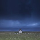 Maison solitaire dans un champ sous un ciel orageux — Photo de stock
