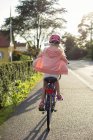 Fille portant un casque rose vélo d'équitation le long de la rue — Photo de stock