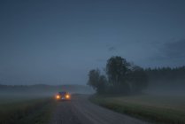 Carro na estrada rural nebulosa ao entardecer — Fotografia de Stock