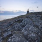 Rocky hill and lit up lighthouse at dusk — Stock Photo