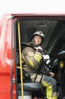 Mulher bombeira sentada no carro de bombeiros e olhando para cima — Fotografia de Stock