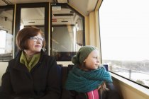 Girl sitting with grandmother in tram and looking through window — Stock Photo