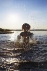 Вид спереду дівчина бризкає в озері на заході сонця — стокове фото