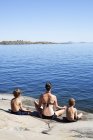 Vista trasera de la madre y los hijos practicando yoga en la playa - foto de stock