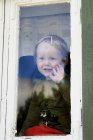 Vista frontal do menino olhando através da janela — Fotografia de Stock