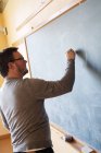 Rear view of teacher writing on blackboard — Stock Photo