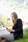 Mujer joven mensajes de texto en el teléfono inteligente en el parque - foto de stock