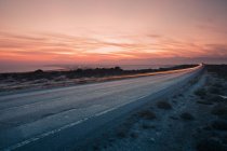 View of light trail on road by sea at sunset — Stock Photo