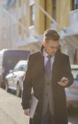 Businessman texting in sunlit street, focus on foreground — Stock Photo