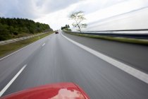 Borrosa toma de movimiento de coche rojo recortado montar en carretera asfaltada - foto de stock