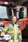 Sonriente bombero femenino sosteniendo casco por camión de bomberos - foto de stock