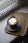 Wooden board with cup of latte on windowsill — Stock Photo