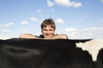Smiling farmer posing with arms on cows back — Stock Photo