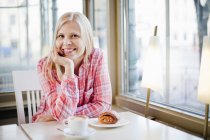 Femme à la table de café souriant et regardant la caméra — Photo de stock