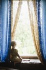Дівчина з білявим волоссям дивиться через вікно — стокове фото