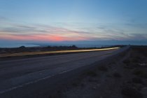 Sentier lumineux sur la route sous un ciel nuageux au coucher du soleil — Photo de stock