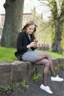 Молодая женщина пишет смс в парке, избирательный фокус — стоковое фото