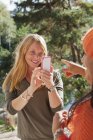 Woman photographing friend with smartphone, selective focus — Stock Photo
