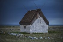 Vue de face de la maison avec toit de chaume dans le champ au crépuscule — Photo de stock