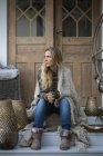 Blonde woman wrapped in plaid sitting on house porch — Stock Photo