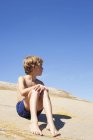 Хлопчик сидить на скелі влітку проти блакитного неба — стокове фото