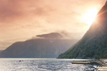 Setting sun behind mountains over calm harbor with motor boat — Stock Photo