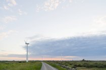 Turbine eoliche e strada rurale sotto cielo nuvoloso tramonto — Foto stock