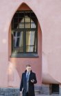 Бизнесмен, стоящий у здания арки и использующий смартфон — стоковое фото