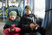 Девушка с отцом сидит в трамвае и пользуется смартфонами — стоковое фото