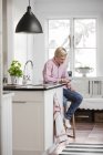 Teenage boy text messaging in kitchen — Stock Photo