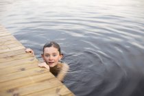 Front view of boy in lake touching wooden jetty — Stock Photo